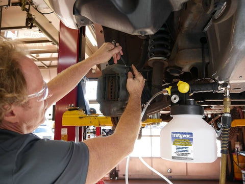 Mechanic using Pro Grade Hydraulic Brake And Clutch Bleeding Kit For Cars, Trucks, SUVs And Motorcycles with air-operated reservoir