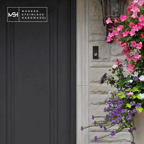 Sick Modern Stainless Doorbell Black R7 Series with Anodized Aluminum Button on stone wall with flowers