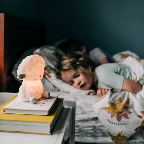 Night Light For Kids Sleep Aid With Sleepy Sheep Audio Play Character on bedside table, child sleeping in background