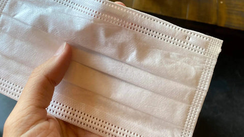 Hand holding Made In USA 3 Layer Disposable Face Masks Bulk Pack 500 Count 6.69 Inches Long By 3.74 Inches Wide With Ear Loop Medical Procedure Masks And Meltblown Filter Layer.