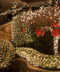 Clear Warm White Outdoor Christmas String Lights On White Wire 150 Count Incandescent Mini Lights 120V UL Certified End To End Connectable illuminating a garden with holiday ornaments.