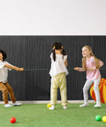 Children playing with a string in front of 6 Pack Acoustic Wall Panels 47.2 By 23.6 Inches Black Sound Proof Panels.
