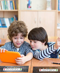 Two children using a tablet at desks labeled with 48 Desk Name Tags Classroom Set With Traditional Manuscript Nametags.