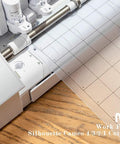 Nicapa 12x12 inch standard-grip cutting mat for Silhouette Cameo, shown beside the machine on a wooden desk.