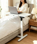 Stylish Electric Height Adjustable Mobile Overbed Side Table With Quiet Lifting Motor, Digital LED Display, Hidden Rolling Wheels, And Sleek Design For Ultimate Comfort And Versatile Usage In Any Bedroom Or Home Office Setup Today. A user working on a laptop.