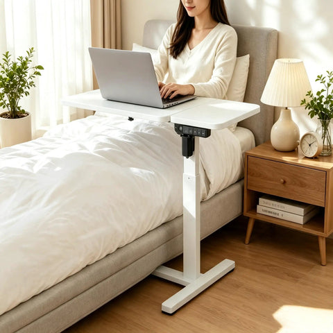 Stylish Electric Height Adjustable Mobile Overbed Side Table With Quiet Lifting Motor, Digital LED Display, Hidden Rolling Wheels, And Sleek Design For Ultimate Comfort And Versatile Usage In Any Bedroom Or Home Office Setup Today. A user working on a laptop.