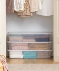 Heavy Duty 50 Quart Stackable Plastic Storage Bins With Snap Tight Secure Lids Clear Organizers For Home Office Dorm Room Garage No Sweat Bulk Pack Of Three with folded clothes in a closet.