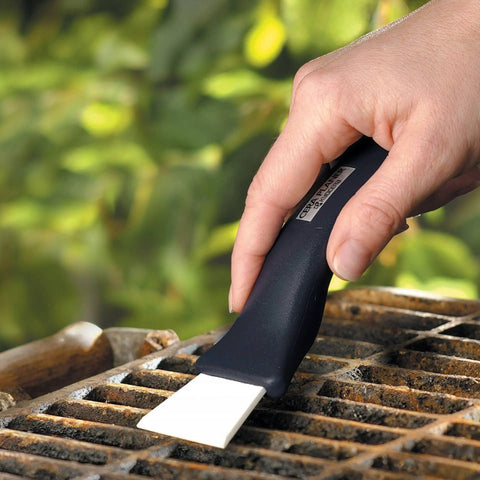 Hand using Ceramic Utility And Barbecue Scraper For Home And Kitchen Surfaces, Durable Ceramic Blade For Removing Paint, Lacquer, Mildew, Or Rust on grill
