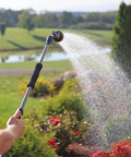 Person using RelaxGrip No Sweat Eight Pattern Pivoting Head Watering Wand with Quick Connect, extending water spray over garden plants