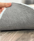 Close-up of a hand lifting the Non Slip Rug Pad Runner Two Point Five By Nine Feet Thick Quarter Inch Felt And Rubber Duo Lock Grip showing grey texture.