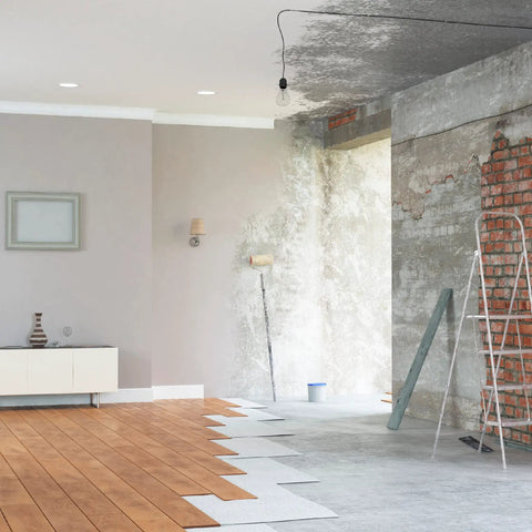 Home improvement project with half-finished flooring, exposed brick, and a paint roller against a partially painted wall.