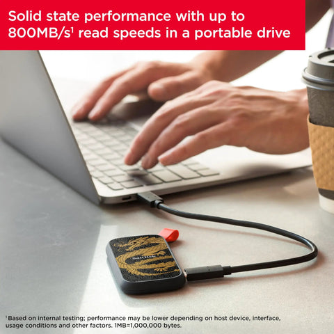 Dragon Edition 1TB Portable SSD with USB-C connected to a laptop, shown on a table next to a coffee cup