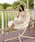 Woman sitting in Swing Egg Chair With Stand For Indoor Outdoor Use, durable wicker rattan basket with UV resistant cushions, beige