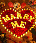 "Marry Me" in lights surrounded by 6000 Artificial Rose Petals And 72 Heart Shaped LED Tealights For Romantic Nights Valentines
