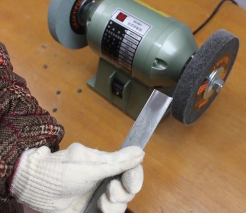 User holding a metal tool near a 6 inch bench grinder equipped with Premium Nylon Deburring Wheels 6 Inch, 180 Grit Silicon Carbide Buffing Pads 5 Pack.