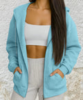 Light Blue Zip Up Hoodie For Women with fleece lining, front view, worn over white top, showing pockets and zipper detail.