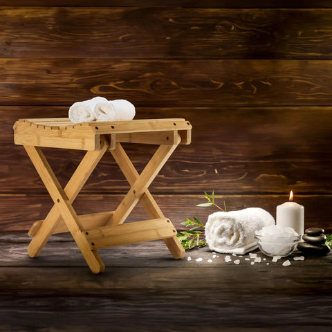 Foldable Shower Stool For Tiny Bathrooms Bamboo Foot Rest And Shaving Stool next to candles, towels, and spa decor.