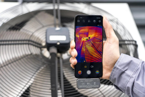 Hand holding Android phone with iSee Mobile Thermal Camera displaying thermal image of a fan, real-time 25Hz imaging for inspections.