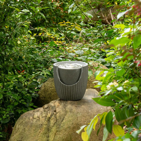 Outdoor Tabletop Water Fountain With LED Lights Made From Recycled Polyethylene Eco Friendly Materials For Patio Porch And Backyard Bubbling Water Feature UV Resistant Durable Yard Decor For All Weather placed on a rock in a garden setting.