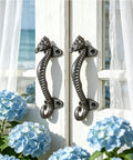 Two Pack Seahorse Cast Iron Door Handles Set on white rustic door, heavy duty pulls for farmhouse, vintage decorative hardware.