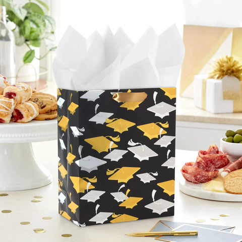 Medium Graduation Gift Bag With Tissue Paper Featuring Gold And Silver Mortarboards On Black for College High School Eighth Grade Kindergarten And Nurses Gift Ready, displayed on a kitchen counter with snacks.