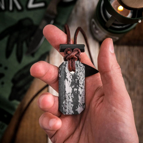 Hand holding Viking Spark Whetstone Sharpener And Fire Starter Necklace, All-In-One Survival Gear with textured design, close-up.