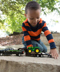 Child playing with Ford F350 Pickup and John Deere Tractor Toy Set with Gooseneck Trailer, 1 to 32 Scale on stone surface outdoors