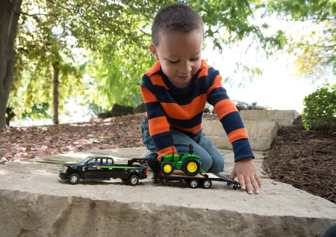 Child playing with Ford F350 Pickup and John Deere Tractor Toy Set with Gooseneck Trailer, 1 to 32 Scale on stone surface outdoors