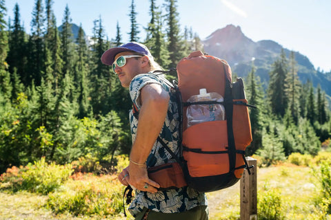 Hiker with backpack in forest carrying Ultralight Two-Liter Collapsible Water Bottle For Camping And Hiking With Screw Cap BPA Free BPS Free