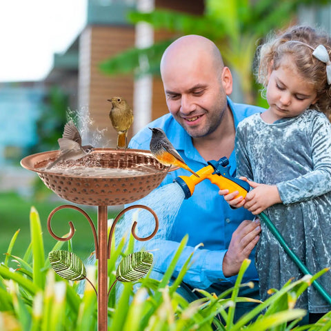 Father and daughter using hose near Vintage Copper Metal Bird Bath Stand for Outdoors with birds in garden setting.