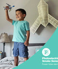 Child playing with toy airplane in bedroom with focus on photoelectric smoke sensor feature advertised in image.