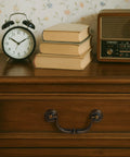 Vintage style bail drop cabinet pull in antique dark brass on wooden drawer with books, clock, and radio on top