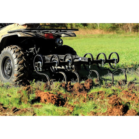 Heavy Duty Atv UTV S Tine Cultivator attached to ATV, breaking compacted soil with six plow points in a grassy field.