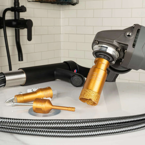 Diamond hole saw bit installed on an angle grinder; orange/gold core drill with textured tip and spare bits nearby.