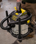 Beast Of A 5 Gallon Wet Dry Shop Vacuum With 4 Peak HP Motor Stainless Steel Tank Portable Vac For Home Garage And Jobsite Dust Cleanup Includes Attachments Silver And Yellow with user gripping the handle on a concrete floor.