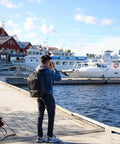 Person wearing Walker Pro 24L Camera Backpack for photography at marina, showcasing dual density straps and urban travel use.