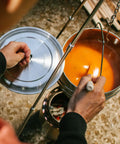 Person cooking with Campfire 2 Pot Wood Burning Camping Stove Set For 4 Plus People, showing soup in metal pot over fire.