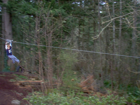 Person using Backyard Zip Line Kit With 100 Foot Cable And Trolley Heavy Duty 350 Lb Capacity Aluminum Handle outdoors in a forest setting