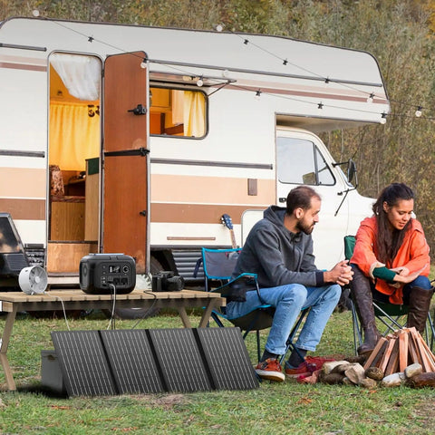 Portable Solar Generator 300W Peak Power Station With 260Wh Battery And 40W Solar Panel Included For Home Use Camping Outdoor Adventures On The Go Off Grid Backup Power in use beside a camper with people sitting around a campfire, highlighting its outdoor capability.