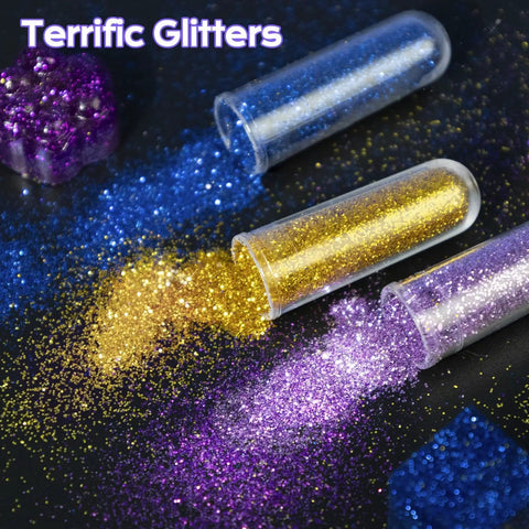 Close-up of blue, gold, and purple glitter spilling from tubes labeled "Terrific Glitters" on a dark background.