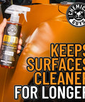 Hand holding Meticulous Matte Detailer And Spray Sealant For Crisp Satin And Matte Finishes Safe For OEM Vinyl And Painted Matte Surfaces 32 Fl Oz Easy Spray Application Non Greasy Matte Coating Streak Free Protection For Your Daily Driver in front of orange matte car finish