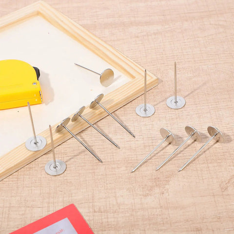 Hella Durable 15 Piece Long Upholstery Nail Set Packed With Heavy Duty Iron Flat Head Push Pins And A Slick Silver Finish displayed on wood.