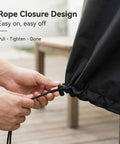 Close-up of hands adjusting rope closure on black heavy duty square patio fire pit and table cover waterproof outdoor furniture cover fits 48 by 48 by 29 inches black durable 420D Oxford fabric keeps rain snow dust off built to last