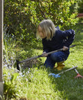 Child using 2 In 1 Garden Hoe Cultivator With 45 Inch Long Handle for weeding and soil loosening in a flower bed.
