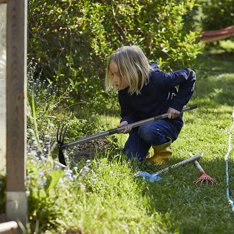 Child using 2 In 1 Garden Hoe Cultivator With 45 Inch Long Handle for weeding and soil loosening in a flower bed.