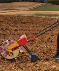 Person using Metal Garden Push Seeder With Seven Seed Holes, No-Bend Labor-Saving Walk-Behind Planter for Row Crops in a field