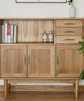 Natural wood cabinet with three doors and two drawers, featuring modern minimalistic design and metal handles, next to a plant.