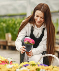 Woman holding a flower in clear 4-inch nursery pot with drainage, in greenhouse setting, showcasing plant pot use.