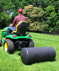 Tow Behind Lawn Roller 690 Lb Capacity With Easy Turn Plug, 36 Inch Wide Poly Drum, attached to a riding mower on a large lawn.