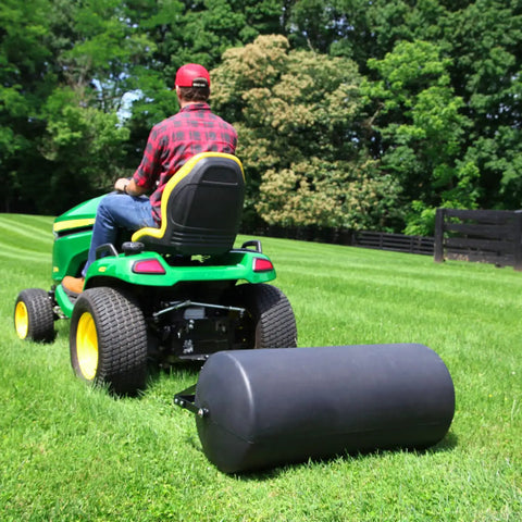 Tow Behind Lawn Roller 690 Lb Capacity With Easy Turn Plug, 36 Inch Wide Poly Drum, attached to a riding mower on a large lawn.